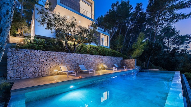 A modern house with a swimming pool, stone wall, and lounge chairs.