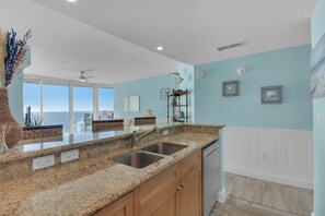 A kitchen with granite countertops, wooden cabinets, a stainless steel sink, and a view of the ocean. - Aqua 1711 - 2B/2 Bath Gulf Front! (Panama City Beach)