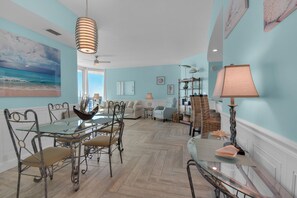 A spacious living room with a large window, a dining area with a glass table, and a cozy seating area with a sofa and armchairs. - Aqua 1711 - 2B/2 Bath Gulf Front! (Panama City Beach)