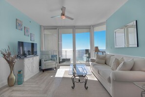 A spacious living room with a balcony, a flat-screen TV, a comfortable sofa, and a glass coffee table. - Aqua 1711 - 2B/2 Bath Gulf Front! (Panama City Beach)
