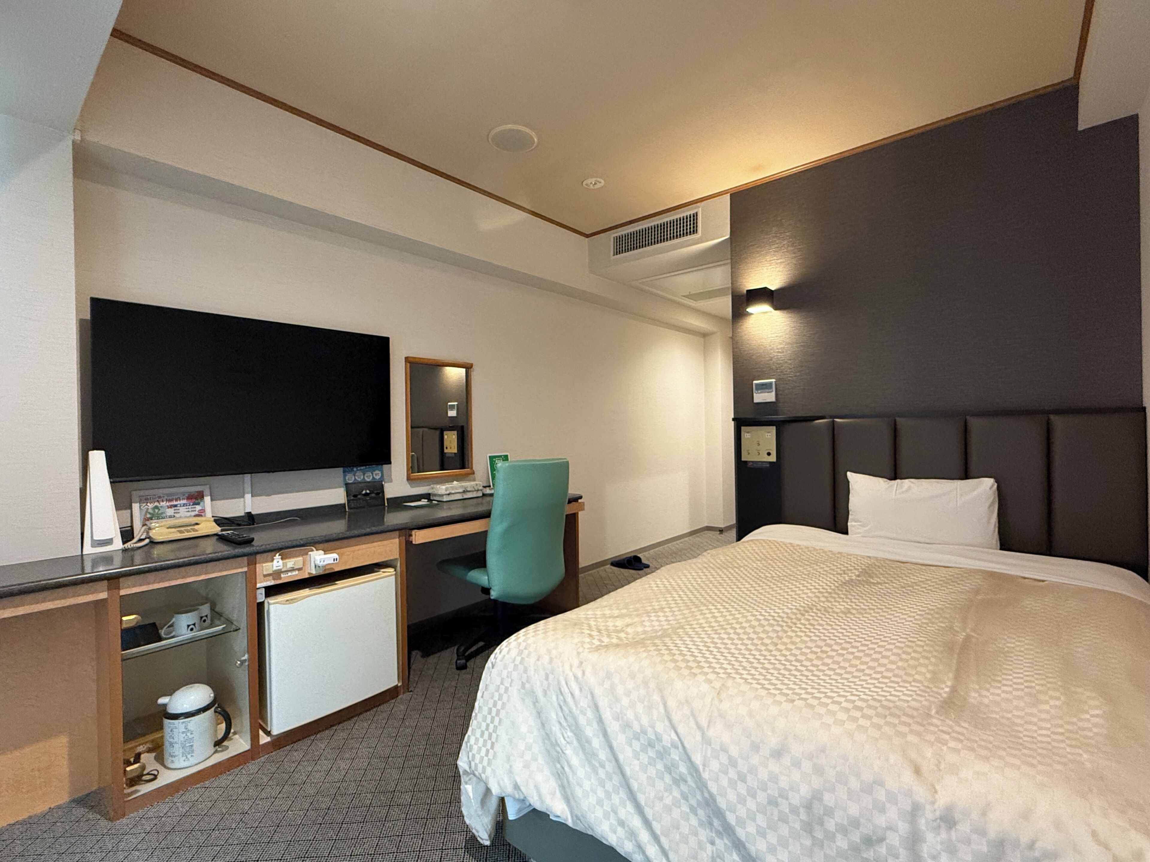 A hotel room with a bed, a desk with a computer, a TV, and a mirror.