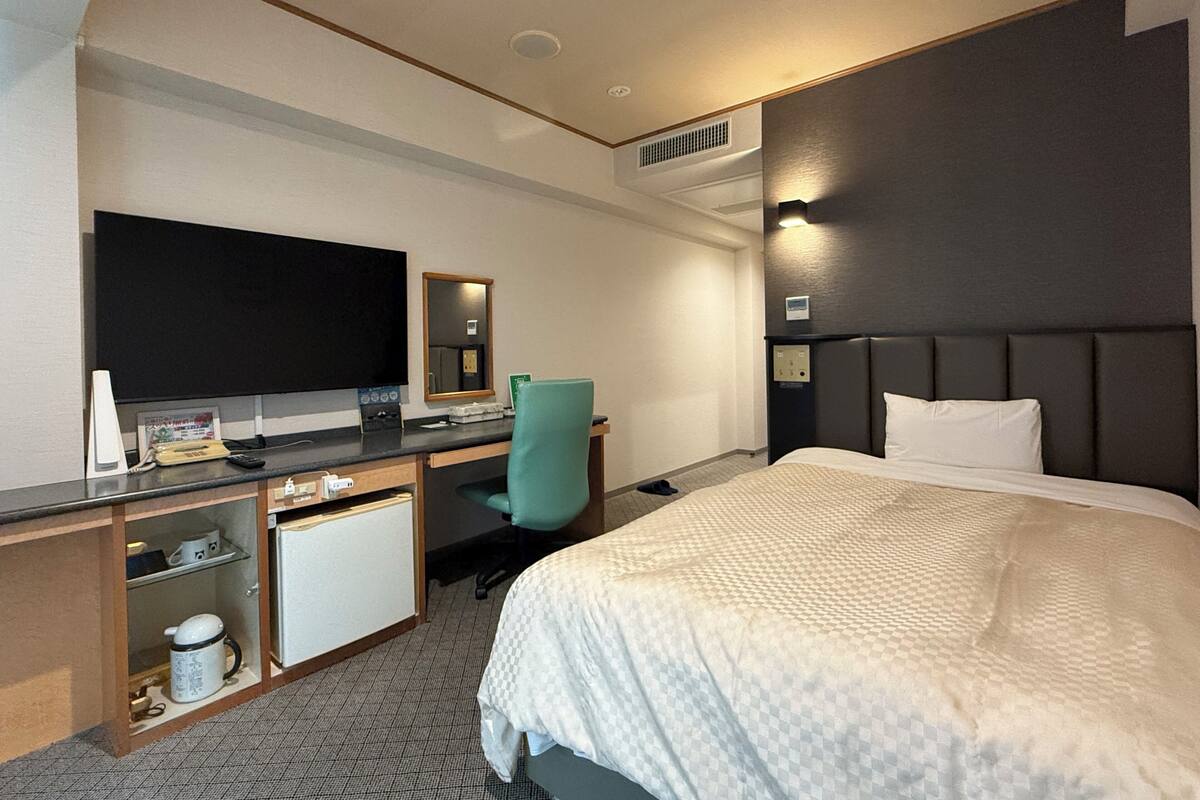 Een hotelkamer met een bed, een bureau met een computer, een televisie en een spiegel.