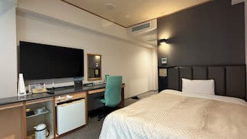 A hotel room with a bed, a desk with a computer, a TV, and a mirror.
