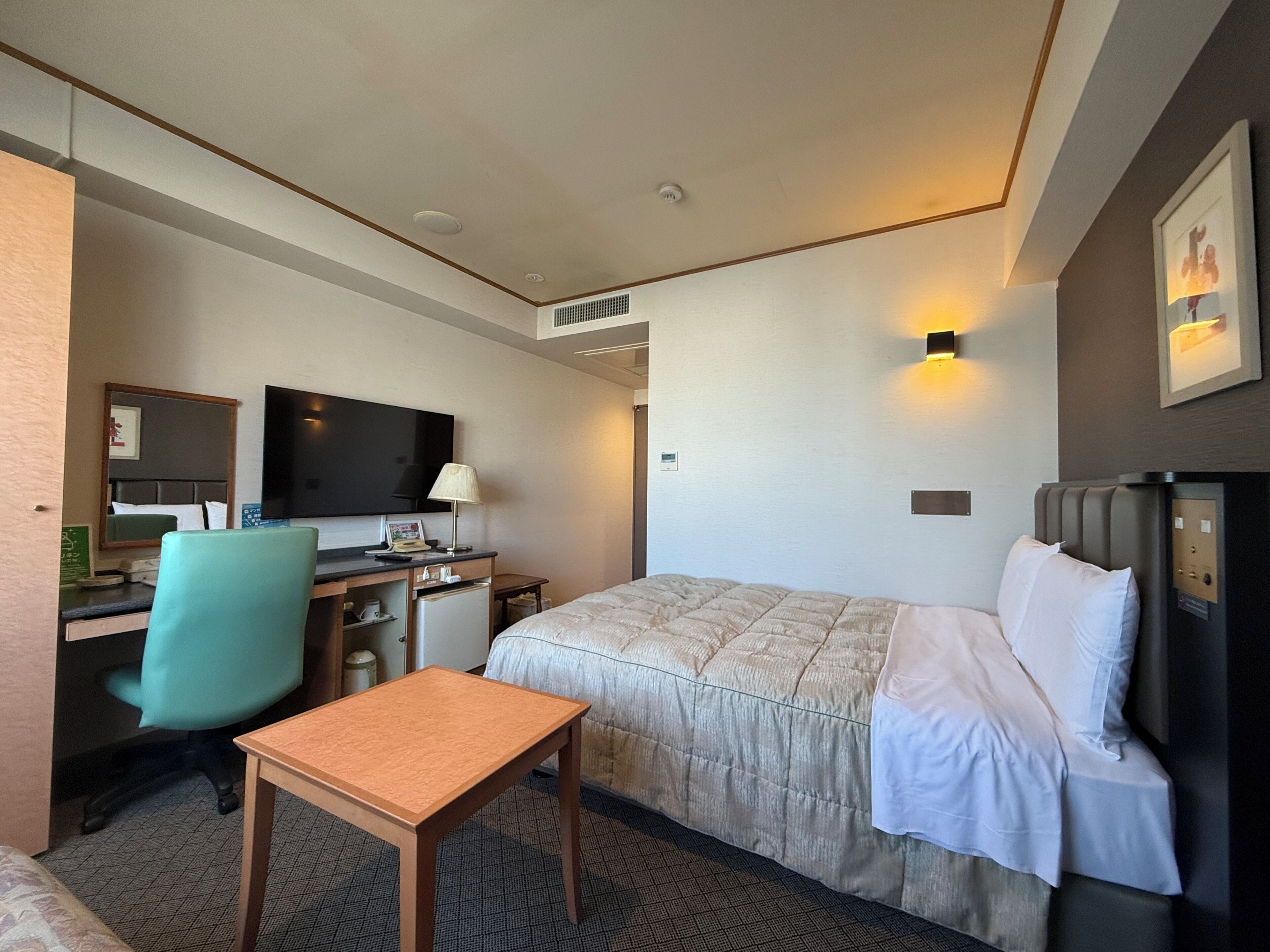 A hotel room with a bed, desk, chair, television, and a small table.