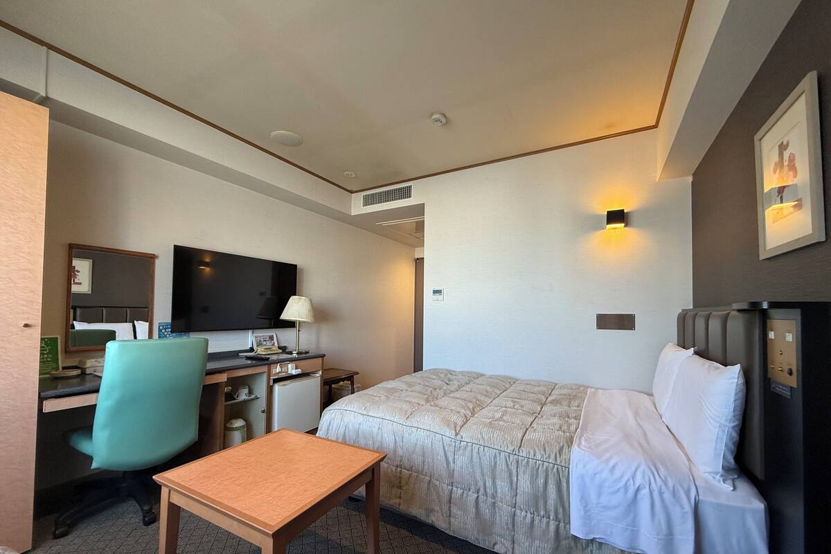 Een hotelkamer met een bed, bureau, stoel, televisie en een klein tafeltje.
