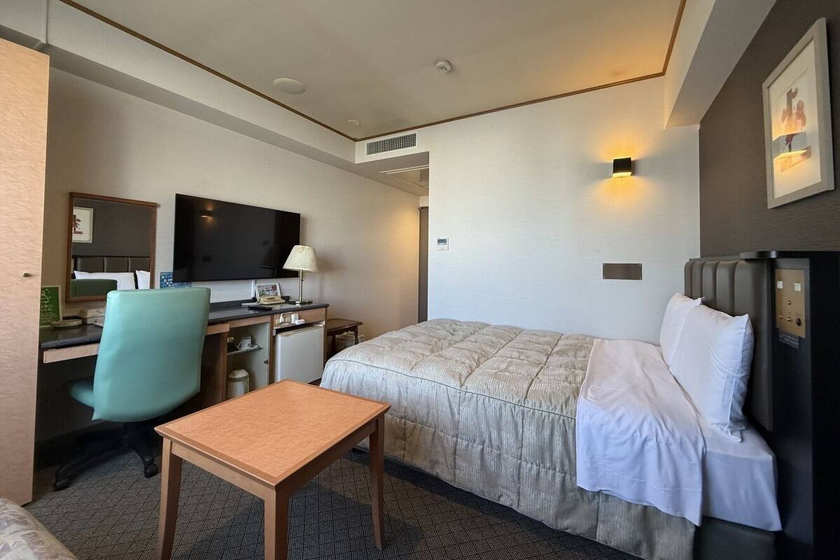 Een hotelkamer met een bed, bureau, stoel, televisie en een klein tafeltje.