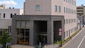 A multi-story hotel with a curved corner, large windows, and a sign reading 'STORIA HOTEL'.