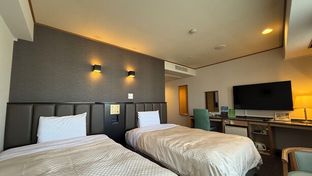 A hotel room with two beds, a desk, a television, and a chair.