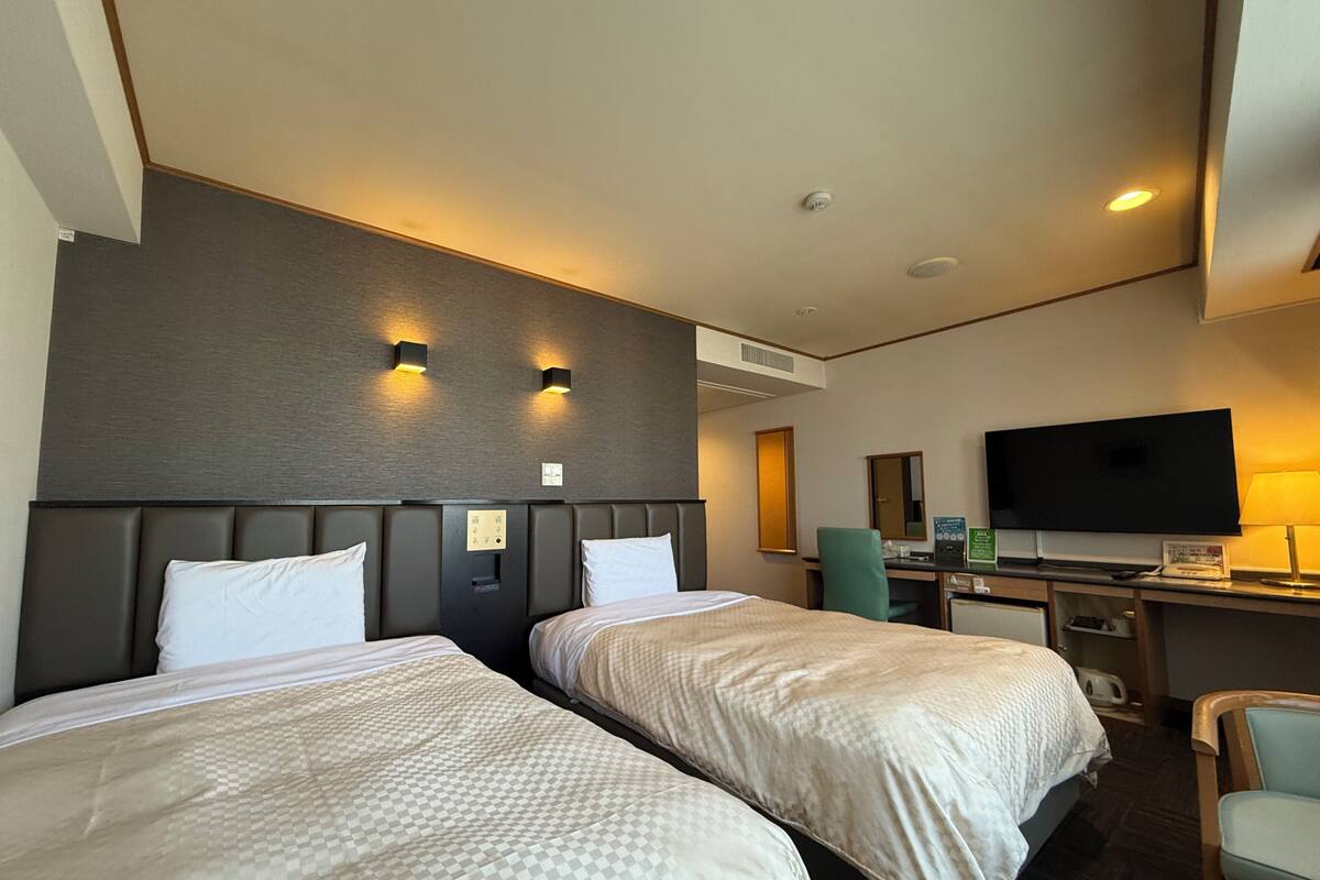 Een hotelkamer met twee bedden, een bureau, een televisie en een stoel.