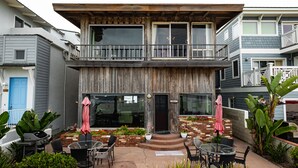 A two-story building with a wooden facade, a balcony, and a patio area with outdoor seating.