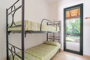 Una cama litera con ropa de cama verde a rayas en una habitación con piso de baldosas y una puerta que da a un espacio al aire libre.