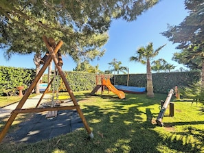 Un parque infantil con columpios y un tobogán, rodeado de césped y árboles.