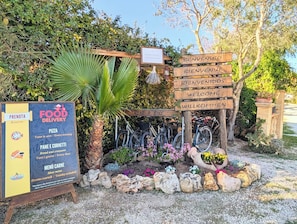 Placa de entrega de comida com cardápio, placa de 'Alugue uma bicicleta' e uma placa de 'Bem-vindo' em vários idiomas.