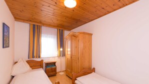 Una camera da letto con due letti di legno, un armadio, un comodino e una finestra con tende.