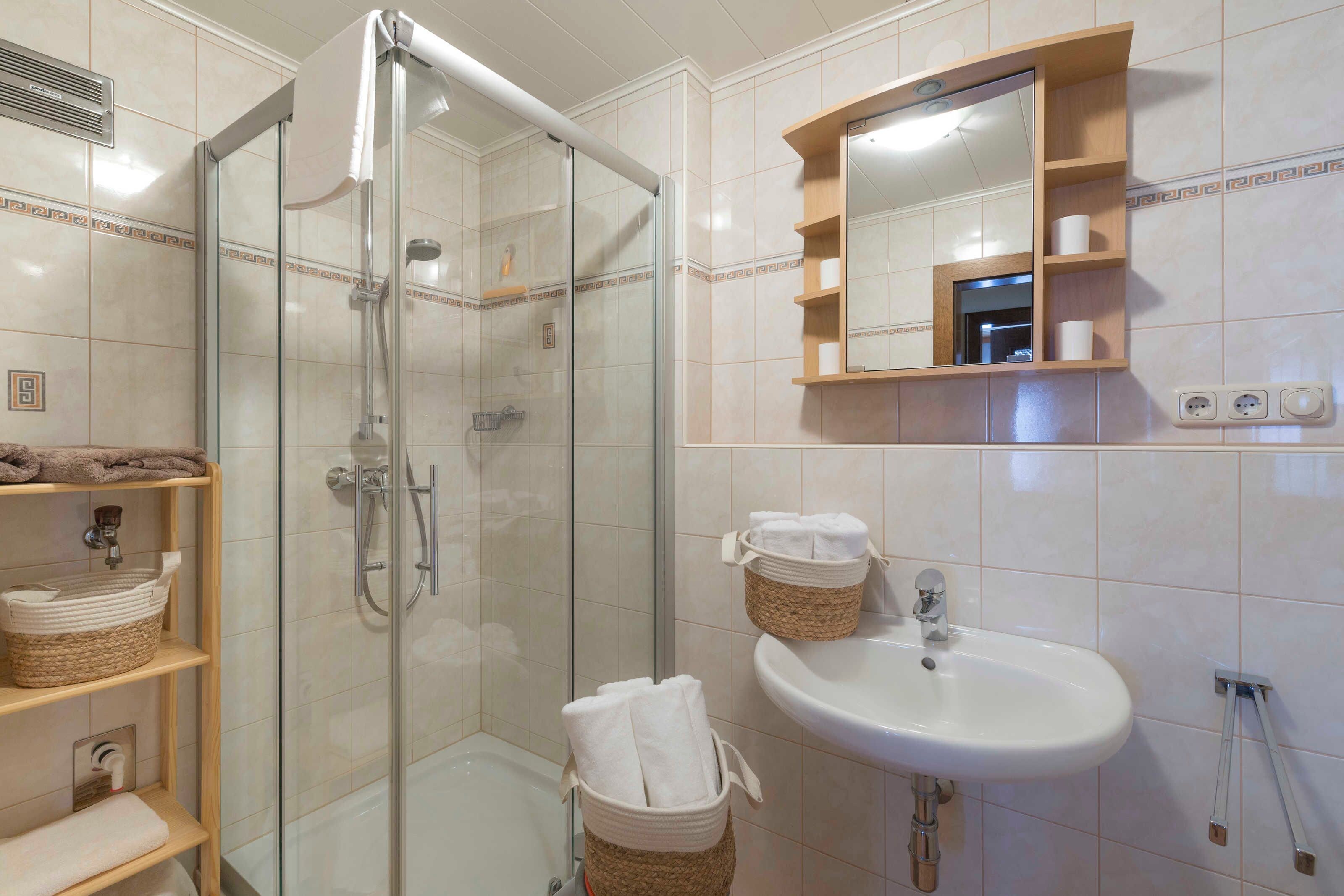 A bathroom with a glass-enclosed shower, a sink with a mirror above it, and shelves with baskets.
