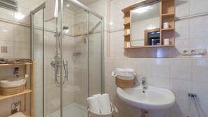 Un bagno con doccia vetrata, lavabo con specchio sopra e scaffali con cesti.