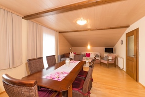 A dining area with a wooden table, wicker chairs, and a view of a living room with a sofa and television. - Apartment Penthouse - Apartment house Roland (Strobl)