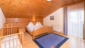 Una camera da letto con soffitto in legno, un letto con biancheria bianca, una piccola culla di legno e una finestra con tende.