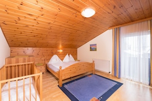 A bedroom with a wooden ceiling, a bed with white bedding, a small wooden crib, and a window with curtains. - Apartment Penthouse - Apartment house Roland (Strobl)