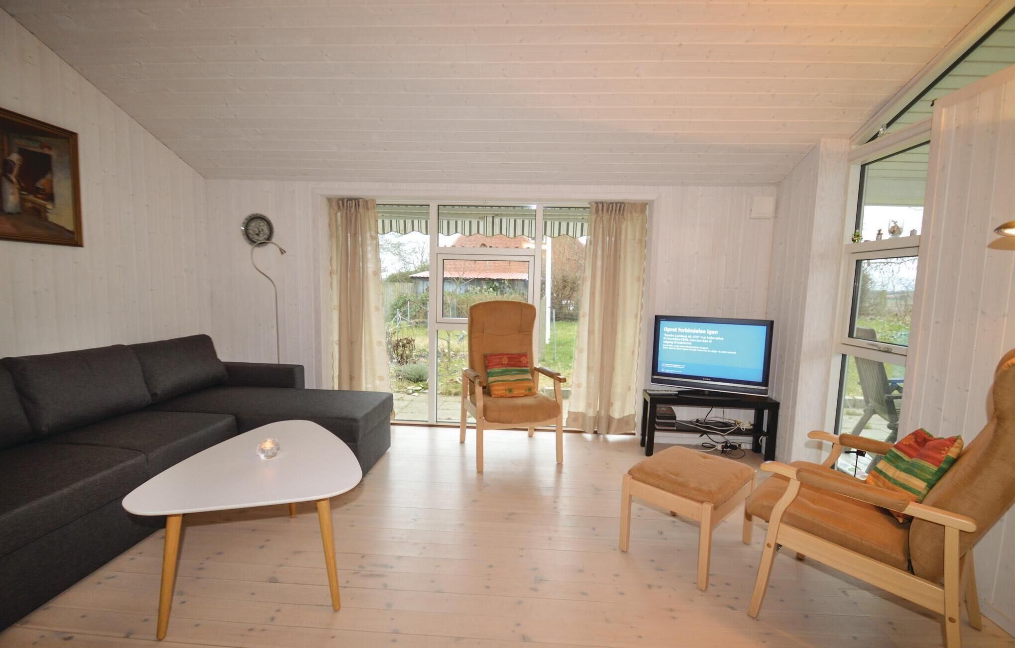 Een woonkamer met een bank, een klein wit tafeltje, een houten stoel, een televisie en een raam met gordijnen.