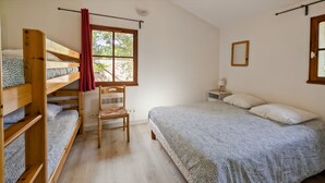 A room with bunk beds, a chair, a bedside table with a lamp, a window with curtains, and a bed with patterned bedding. - Quiet house in exceptionally beautiful Holiday Resort **** in Dordogne-Lot (Gavaudun)