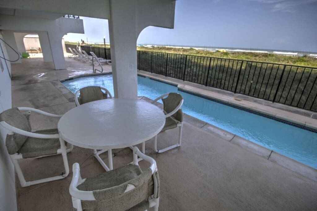 Zona junto a la piscina con mesa y sillas, vista al océano y un paseo vallado.