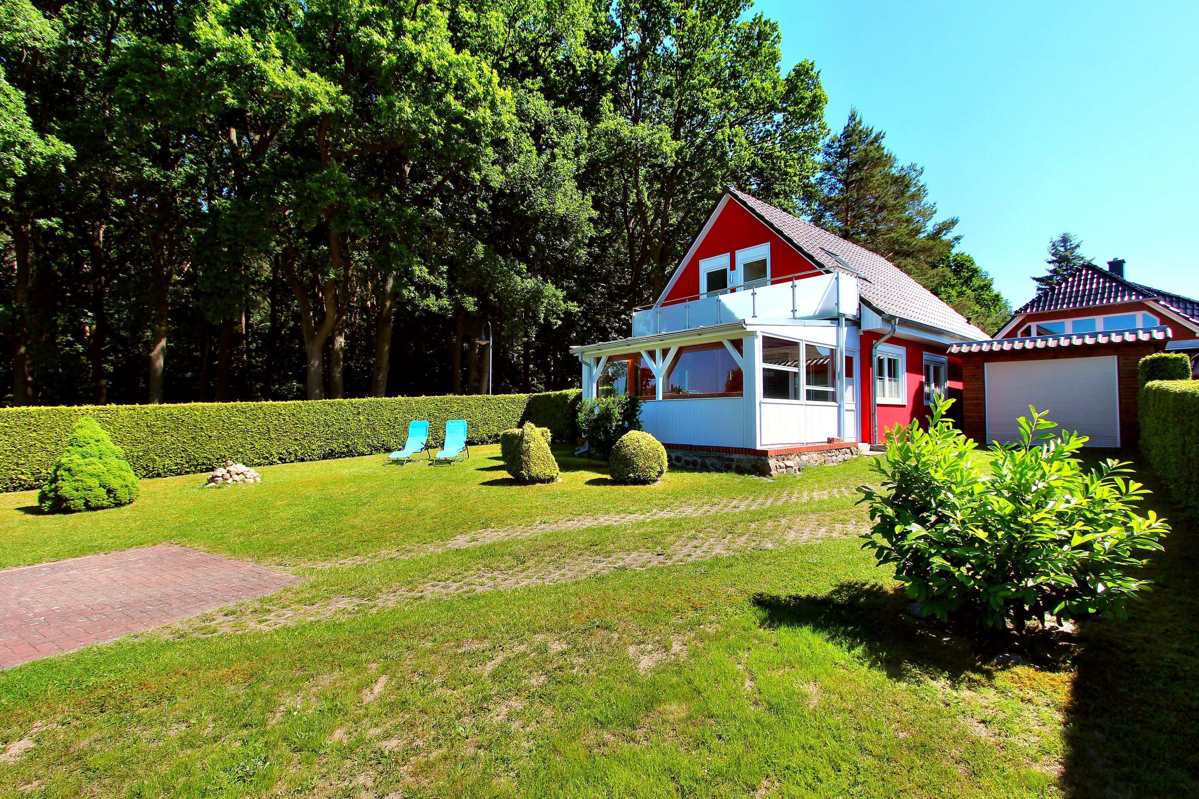 A red and white house with a large garage, surrounded by a well-maintained lawn and hedges.