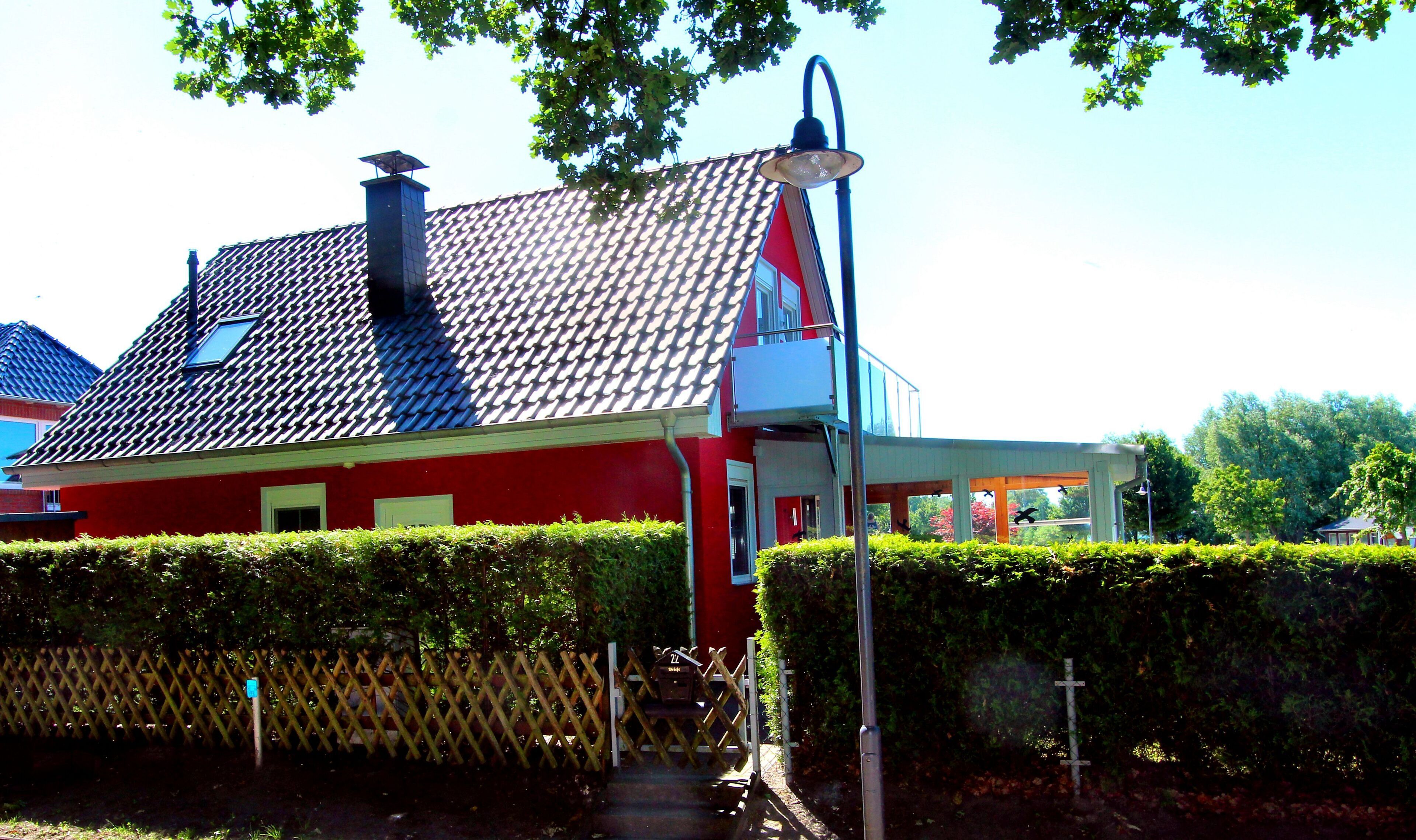 Een rode woning met pannendak, schoorsteen en een klein portaaltje.