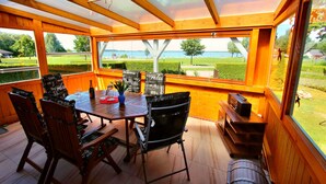 A wooden deck with a table and chairs, overlooking a body of water and a well-maintained lawn. - Holiday home FLOW DREAM - Holiday home FLOW DREAM (Göhren-Lebbin)