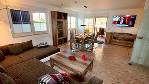 A living room with a sofa, coffee table, and TV. There is a dining area with a table and chairs. - Holiday home FLOW DREAM - Holiday home FLOW DREAM (Göhren-Lebbin)