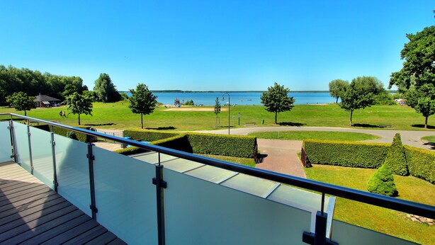 A balcony with a clear view of a landscaped area, a body of water, and distant trees. - Holiday home FLOW DREAM - Holiday home FLOW DREAM (Göhren-Lebbin)