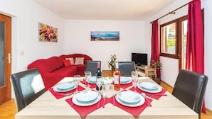 Un coin repas avec une table dressée pour quatre personnes, un canapé rouge, un téléviseur et une fenêtre ornée de rideaux rouges.