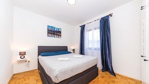 Une chambre à coucher comprenant un lit, une table de chevet, une lampe fixée au mur, un tableau et une fenêtre avec des rideaux.