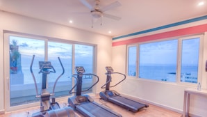 Ett gym med löpband och crosstrainers, stora fönster med utsikt över havet och en takfläkt.