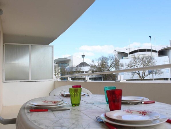 Un balcon avec une table dressée pour le dîner, offrant une vue sur un paysage urbain avec des bâtiments modernes et une tour.