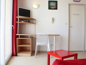 Une pièce comprenant un bureau, une chaise, un téléviseur et une porte portant l’inscription « Chambre ».
