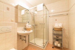 Un bagno moderno con doccia vetrata, un lavabo con un cesto di articoli da toilette e un portasciugamani con asciugamani.