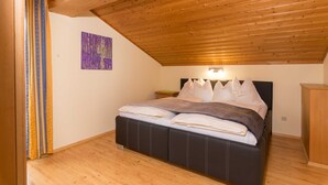 Une chambre avec un plafond en bois, un lit avec une literie blanche et foncée, une table de chevet et une armoire en bois.