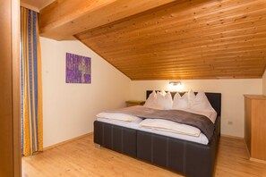 Una camera da letto con soffitto in legno, un letto con biancheria bianca e scura, un comodino e un armadietto in legno.