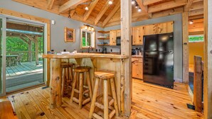 Una cocina rústica con vigas de madera, una zona de bar con taburetes y un refrigerador grande.