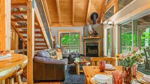 Un interior acogedor de cabaña con escalera de madera, chimenea, sofá y comedor.