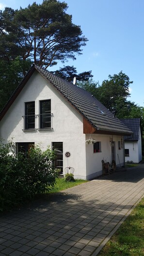 A two-story house with a tiled roof, a front porch, and a small garden area.