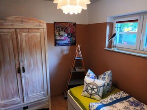 A bedroom with a wooden wardrobe, a bed with patterned pillows, a wall with a 'Hope' poster, a ladder, and a window with a view. - Apartment Hühnergott - Kölp - forest and sea(h)r (Loddin)