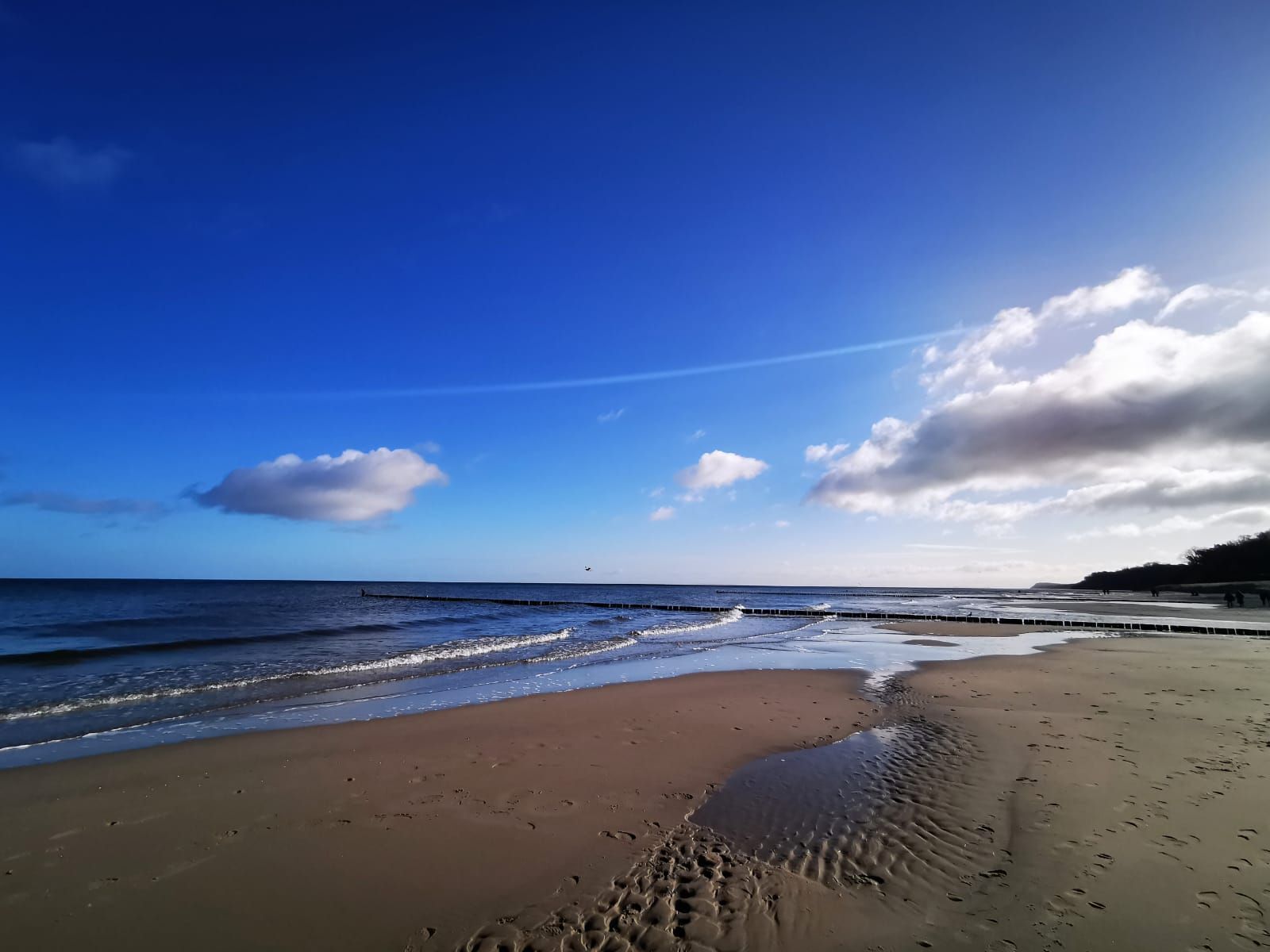 A beach with a clear sky, waves, and footprints in the sand.