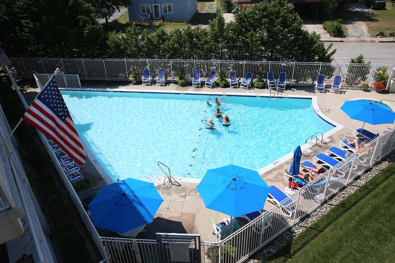 Ein Swimmingpool mit blauen Sonnenschirmen, Liegestühlen und einer amerikanischen Flagge.