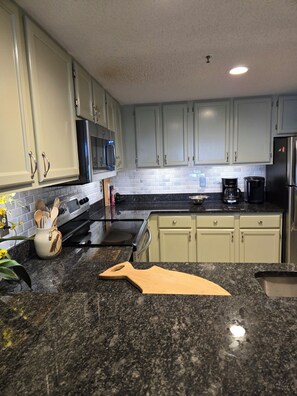 A kitchen with light green cabinets, a black granite countertop, a coffee maker, and a toaster.