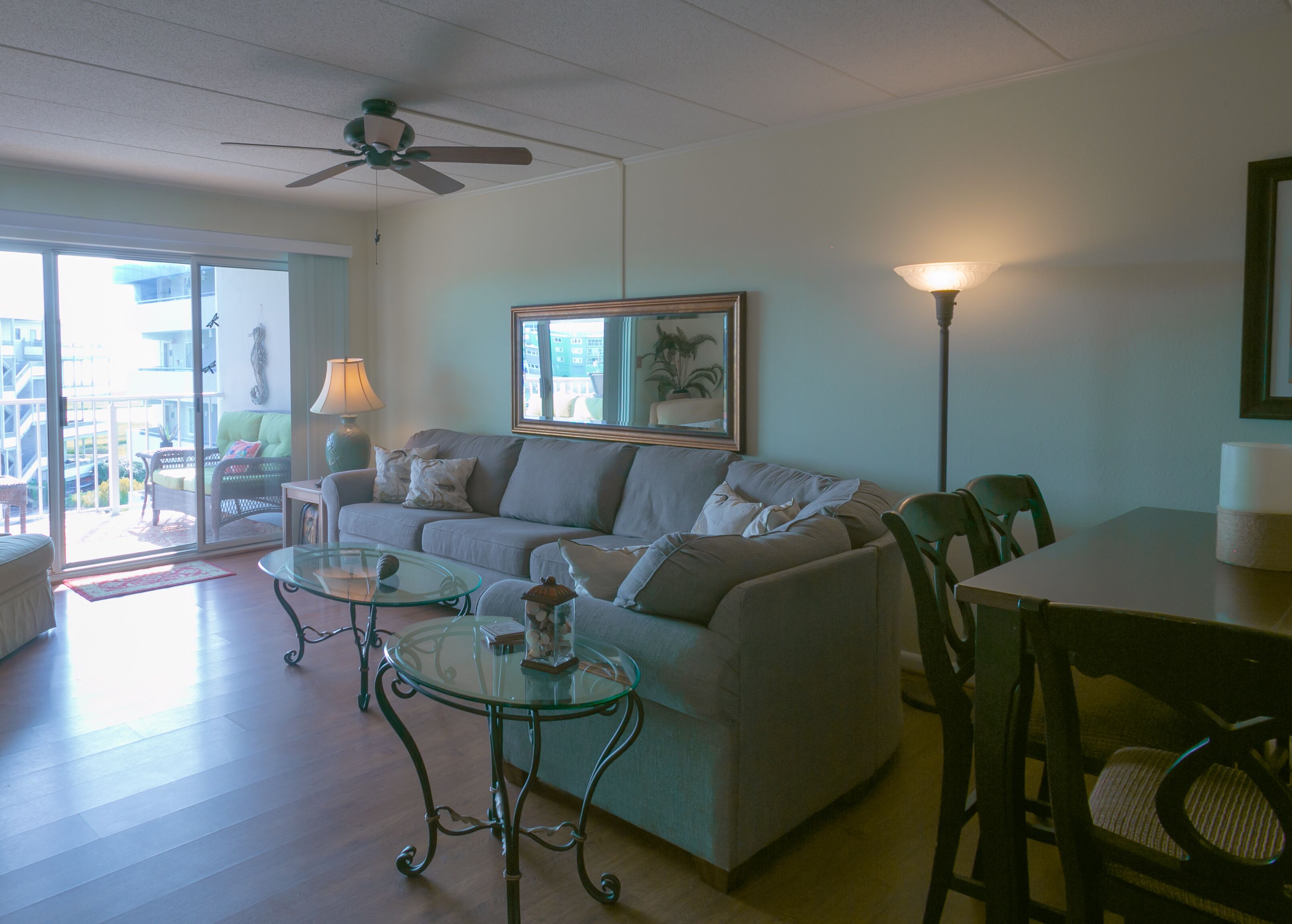 A living room with a sofa, a glass coffee table, a dining table with chairs, a ceiling fan, and a floor lamp.