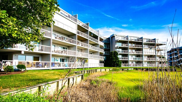 Un immeuble résidentiel à plusieurs étages, doté de balcons, avec une pelouse devant et un ciel bleu dégagé.