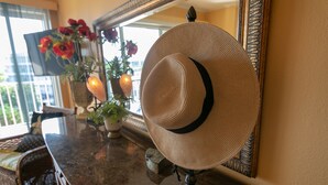 Un chapeau posé sur un présentoir près d’un miroir, un vase avec des fleurs et une chaise.