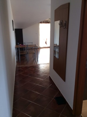 Un pasillo con suelo de baldosas, un comedor con sillas y una mesa, y una puerta con un espejo.